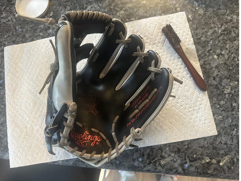 A Rawlings Heart of the Hide glove being cleaned and conditioned with a horsehair brush